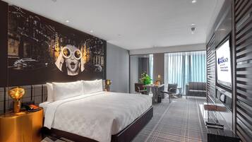 A hotel room with a large bed, a desk, a chair, a small table, and a large window.