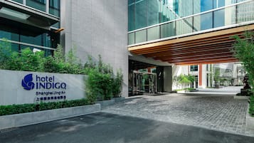 A hotel entrance with a sign, a covered walkway, and a paved area.