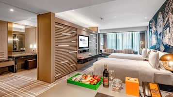A hotel room with a bed, a desk, a television, and a dining area with a tray of fruit.