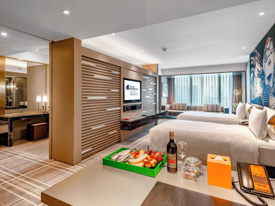 A hotel room with a bed, a desk, a television, and a dining area with a tray of fruit.