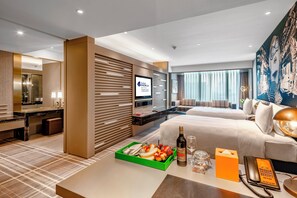 Una habitación de hotel con cama, escritorio, televisor y una zona de comedor con una bandeja de fruta.
