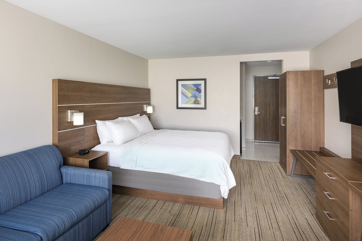 Una habitación de hotel con una cama grande, un sofá azul, un cabecero de madera, un televisor y un cuadro en la pared.