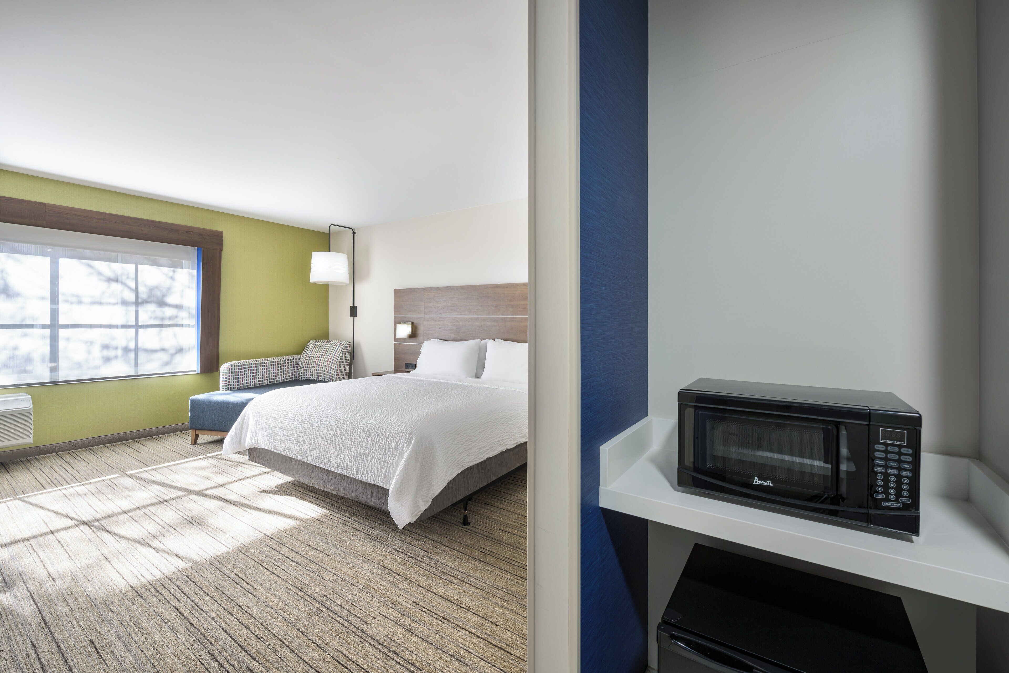 A hotel room with a bed, a window, a microwave, and a small table.