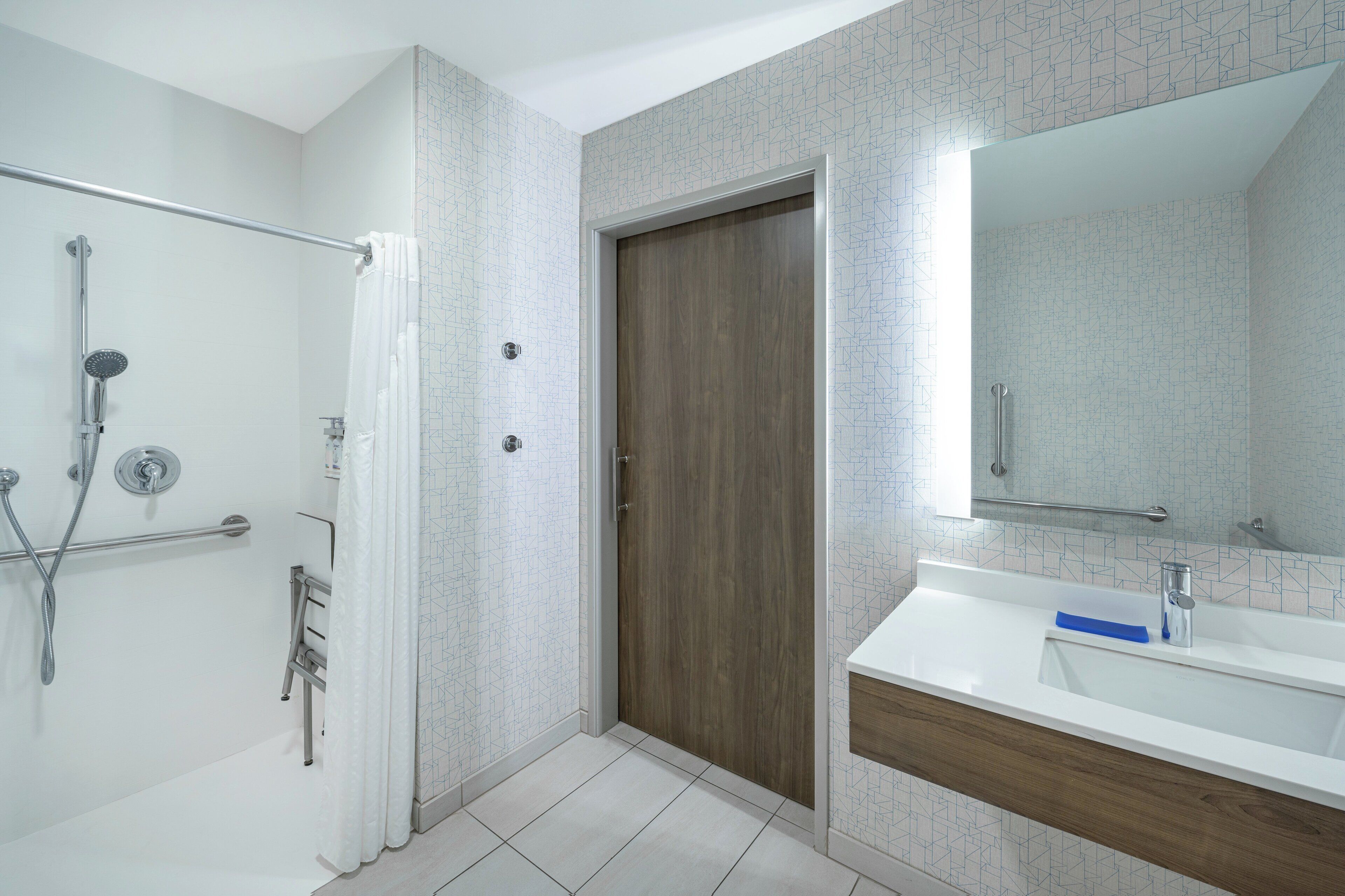 A modern bathroom with a shower, a wooden door, a white sink, and a mirror.