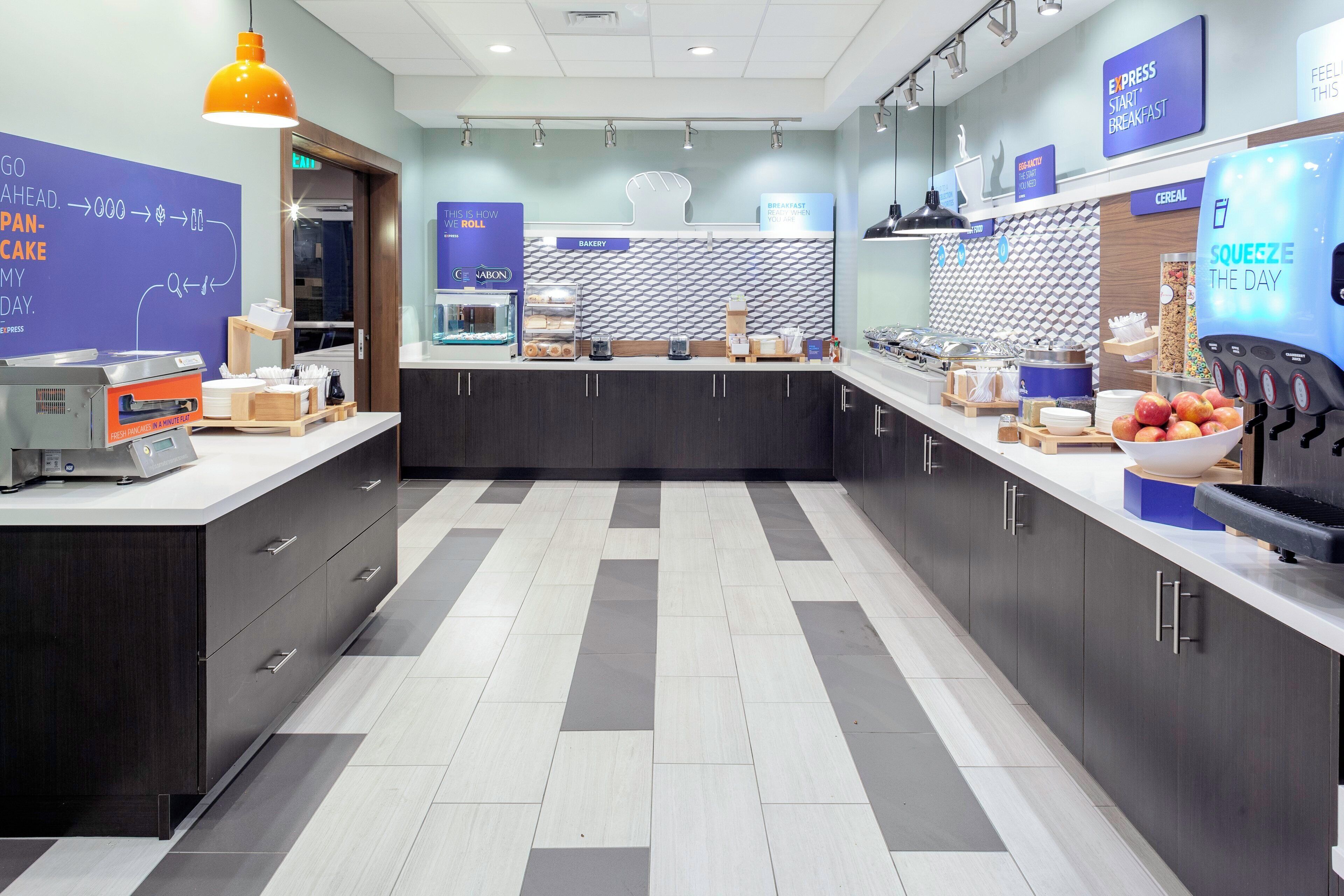 Un área de desayuno moderna con un sector de autoservicio, una exhibición de panadería y un dispensador de zumo.