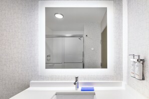 A bathroom with a large mirror, a sink, and a shower.