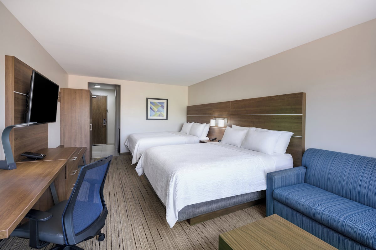 Una habitación de hotel con escritorio, dos camas, un televisor y un sofá azul.