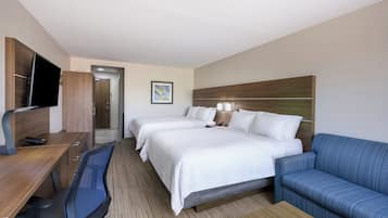 Ein Hotelzimmer mit Schreibtisch, zwei Betten, einem Fernseher und einem blauen Sofa.
