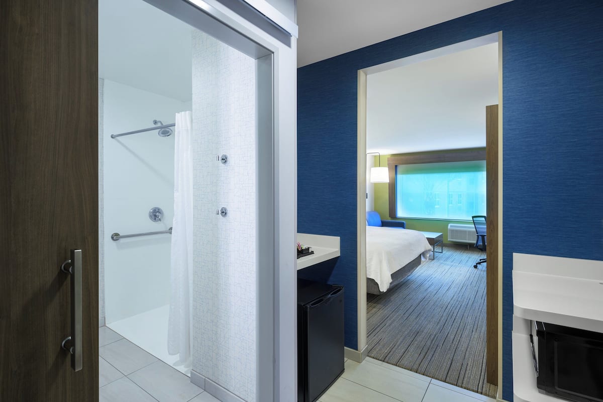 Habitación de hotel con ducha, cama, un escritorio pequeño y vista a la ciudad.