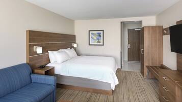 Una habitación de hotel con una cama grande, un sofá azul, un cabecero de madera, un televisor y un cuadro en la pared.