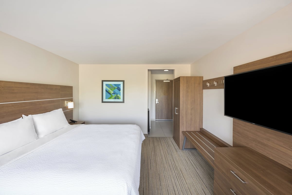 Una habitación de hotel con una cama grande, televisión, armario y un cuadro en la pared.