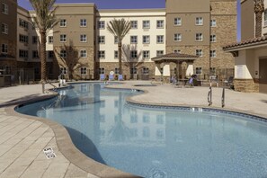 A pool area with a curved design, surrounded by a stone patio and a multi-story building with balconies.