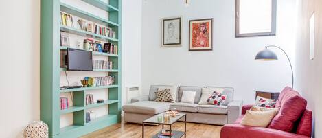 A living room with a bookshelf, a grey sofa, a red armchair, and a coffee table.