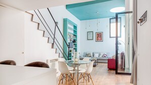 Una sala de estar moderna con una mesa de comedor de vidrio, sillas blancas, un sofá rojo y una estantería azul aguamarina.