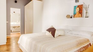 Un dormitorio con una cama grande, un cuadro en la pared y un baño a la vista a través de una puerta abierta.