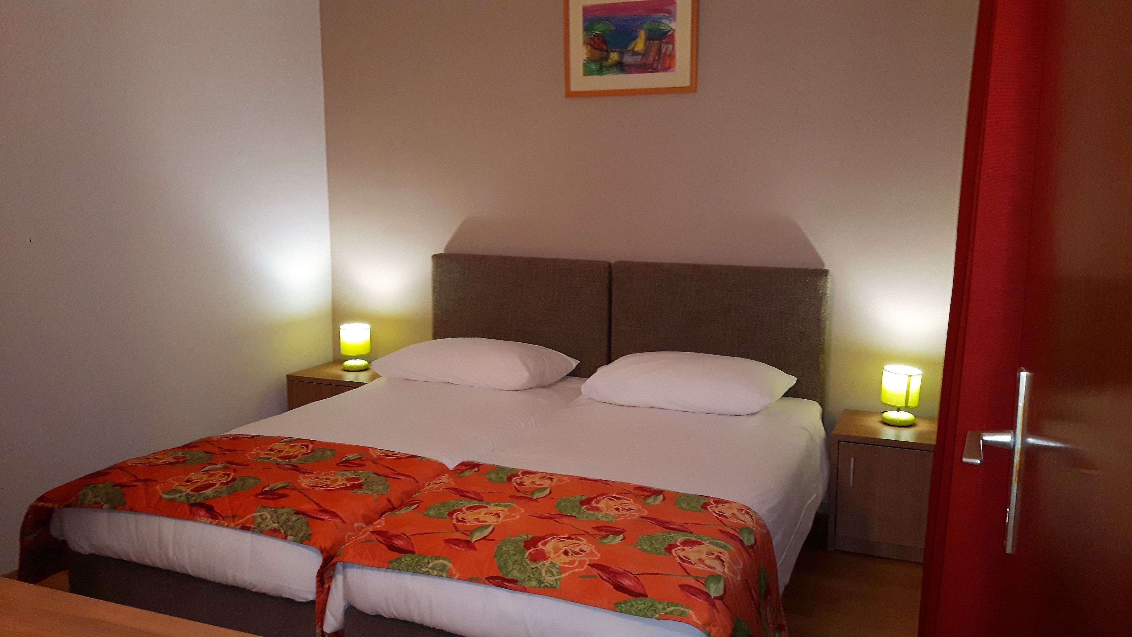 A double bed with two pillows, a nightstand with a lamp, and a door to the right.