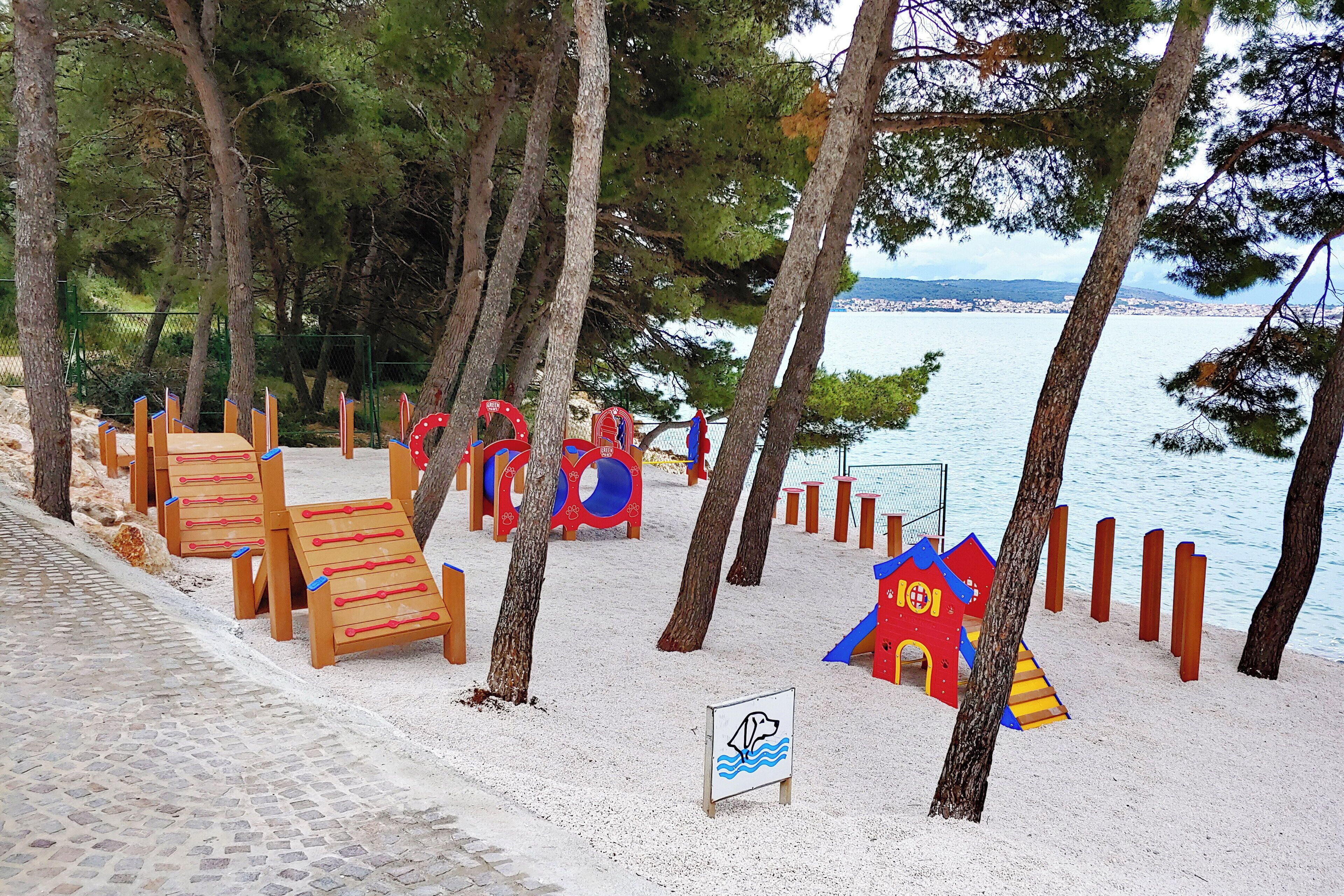 Un’area giochi sulla spiaggia con strutture di legno, una piccola casetta rossa e un cartello che segnala una zona per nuotare.