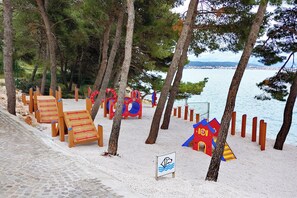 A beachside playground with wooden play structures, a small red house, and a sign indicating a swimming area. -  Amadria Park Camping Trogir - Apartments (Seget)