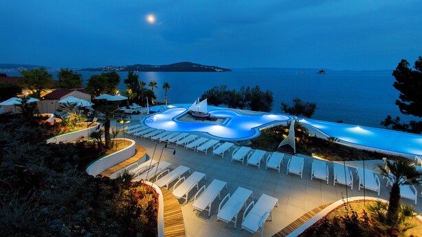 A resort pool with lounge chairs and a boat, surrounded by trees and overlooking the sea. -  Amadria Park Camping Trogir - Apartments (Seget)