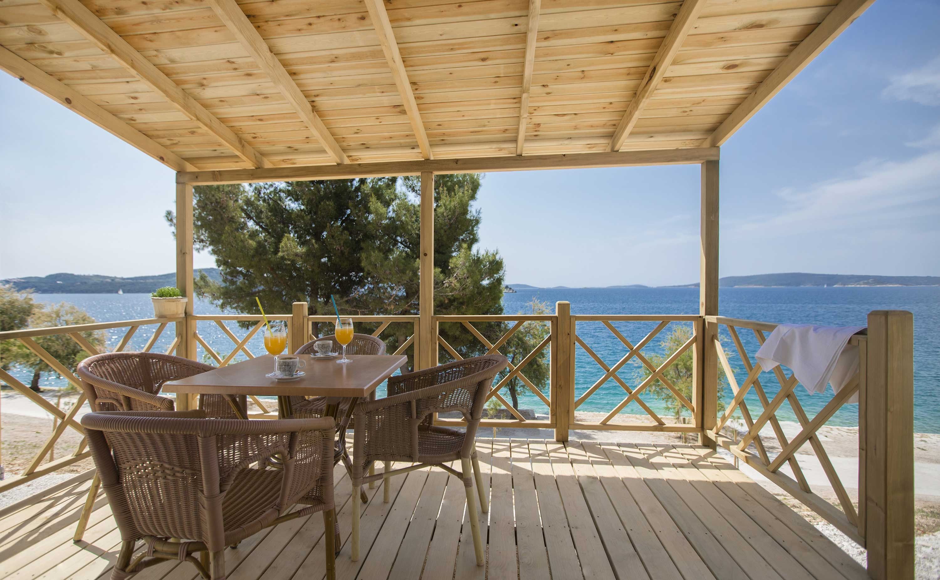 A wooden deck with a table and chairs, overlooking a beach and the sea.
