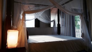 A room with a bed under a canopy, a nightstand with a lamp, and a window with curtains.