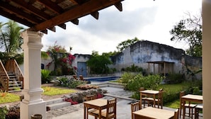 An outdoor patio with wooden tables and chairs, a stone fountain, and a pool.