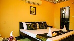 Habitación de hotel con cama, almohadas, toalla, aire acondicionado, un cuadro en la pared y un espejo.
