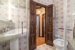 A bathroom with a sink, bidet, and wooden doors leading to a hallway. - Trevi's Roof Terraces (Rome)