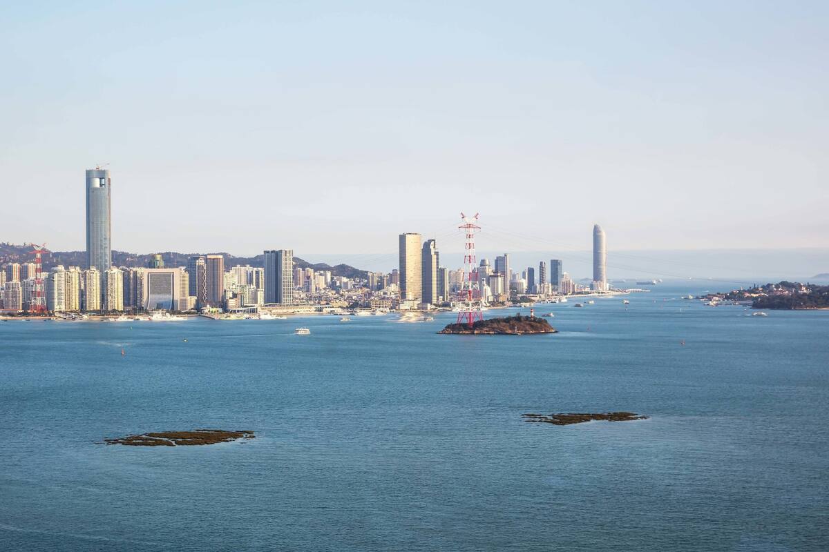 Un paisaje urbano costero con edificios altos, un puerto deportivo con barcos y un cielo despejado.