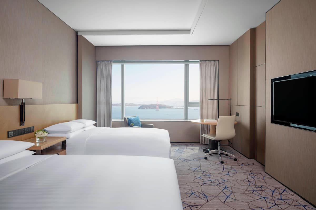 Habitación de hotel con dos camas, televisión, escritorio y vista a un puente.