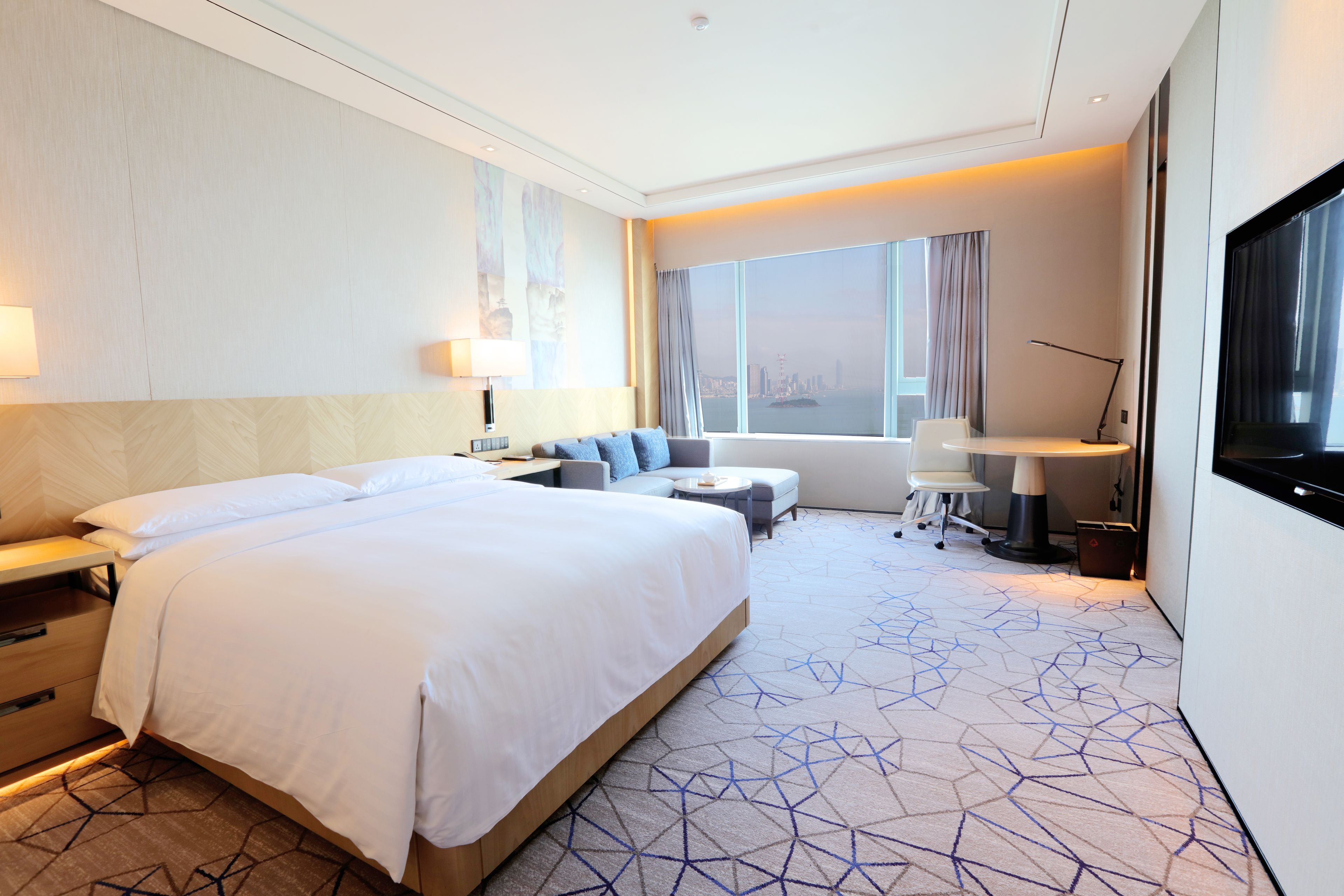 A hotel room with a large bed, a desk, a chair, a sofa, and a TV.