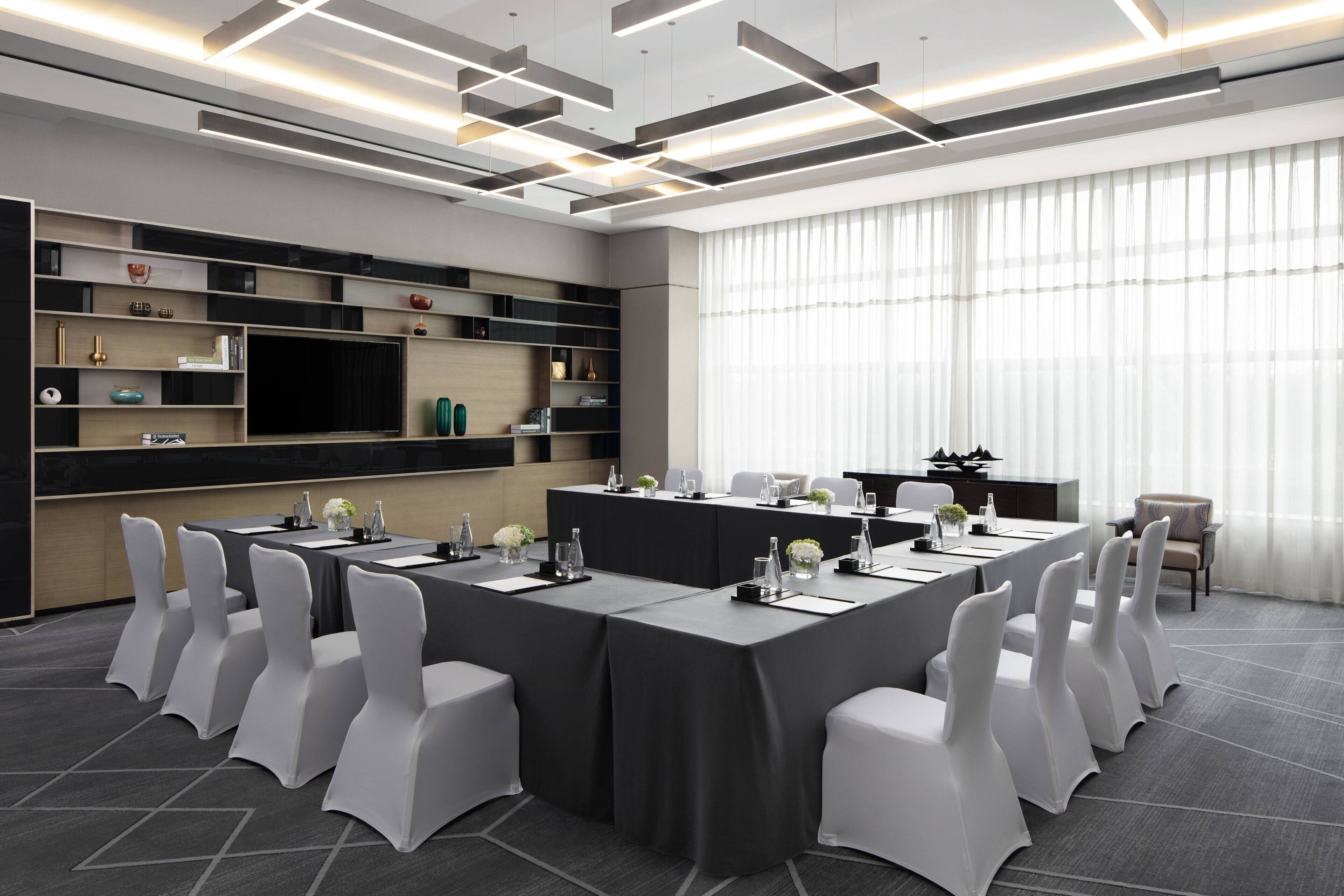 Un salón de conferencias moderno con una larga mesa, sillas blancas y una paleta de colores neutros.