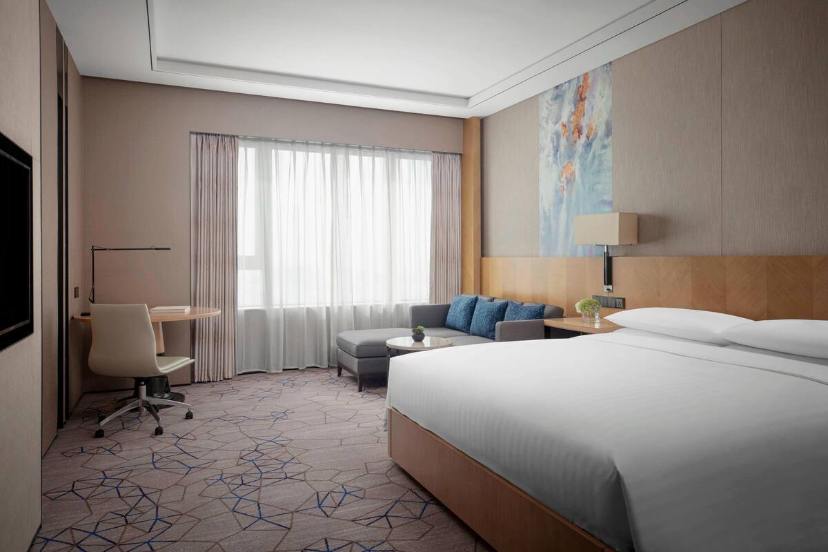 Habitación de hotel con una cama grande, un escritorio, una silla, un sofá y una ventana con cortinas.