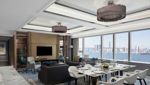 Un salon moderne doté d’un grand téléviseur, de sièges confortables, d’un coin repas pouvant accueillir six personnes et offrant une vue sur la ville grâce à de grandes fenêtres.