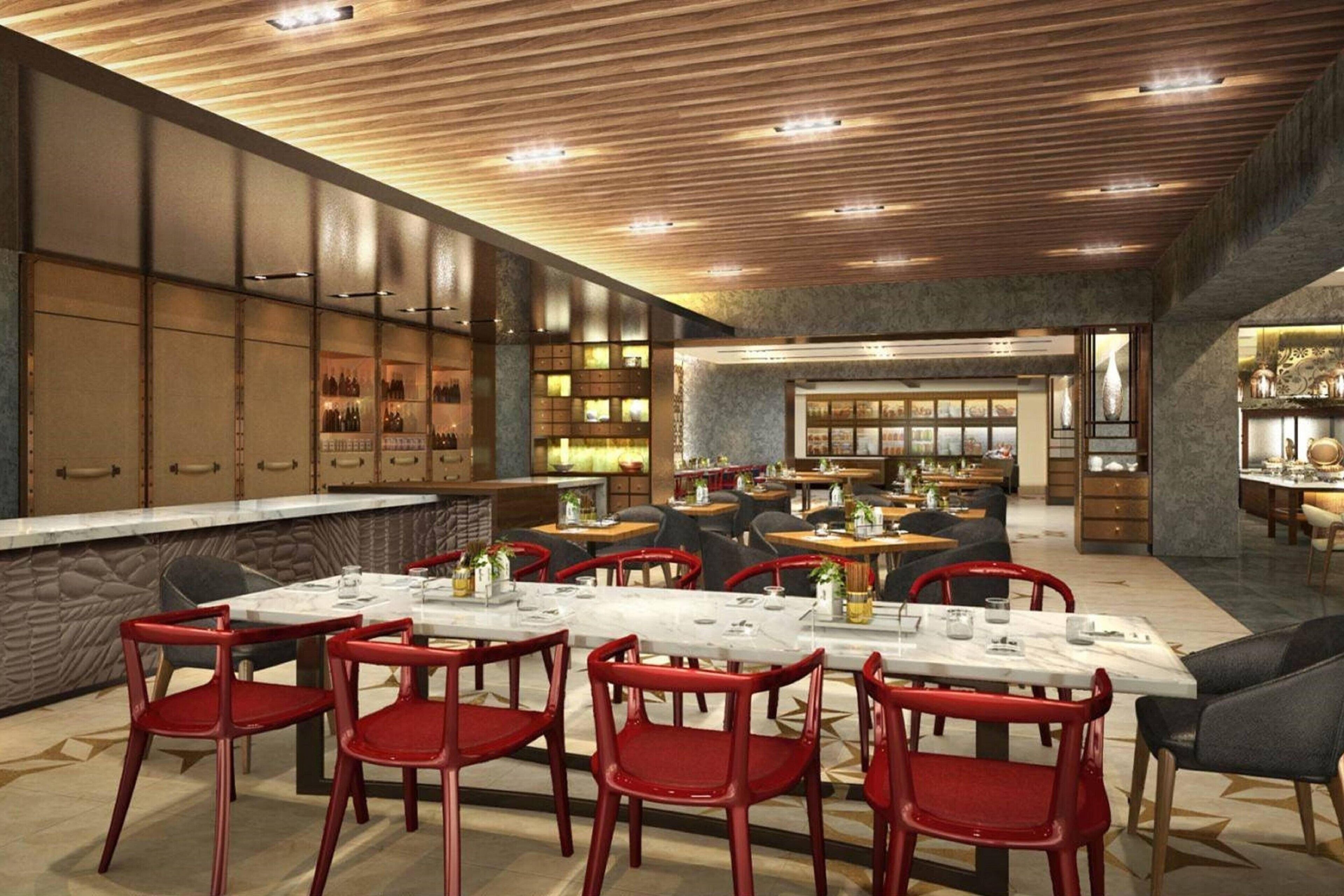 Um restaurante espaçoso com várias mesas de jantar e cadeiras vermelhas, um bar com garrafas e um design moderno no teto.