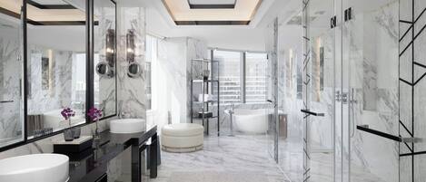 A modern bathroom with marble walls, a large mirror, two sinks, a bathtub, and a glass shower enclosure.