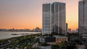 Un hôtel moderne à la façade incurvée, situé près du bord de l’eau et offrant une vue sur les gratte-ciel de la ville.