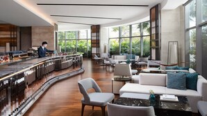 Un espace bar moderne doté d’un comptoir incurvé, de sièges avec des coussins blancs et bleus, et de grandes fenêtres offrant une vue sur la verdure.
