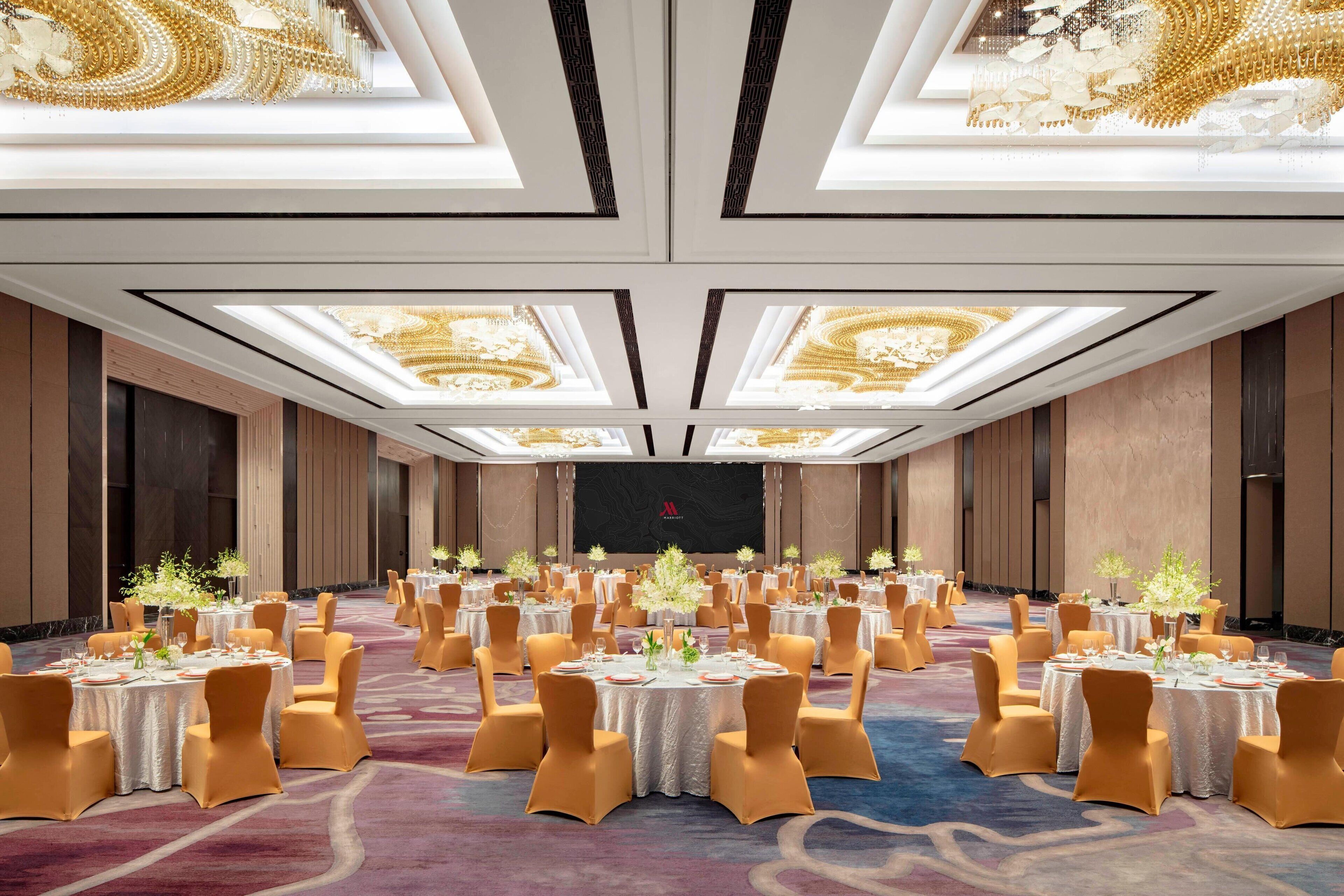 Un salón de banquetes con mesas redondas, sillas y un escenario.