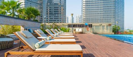 Zona de piscina en la azotea con tumbonas y vistas a edificios altos.