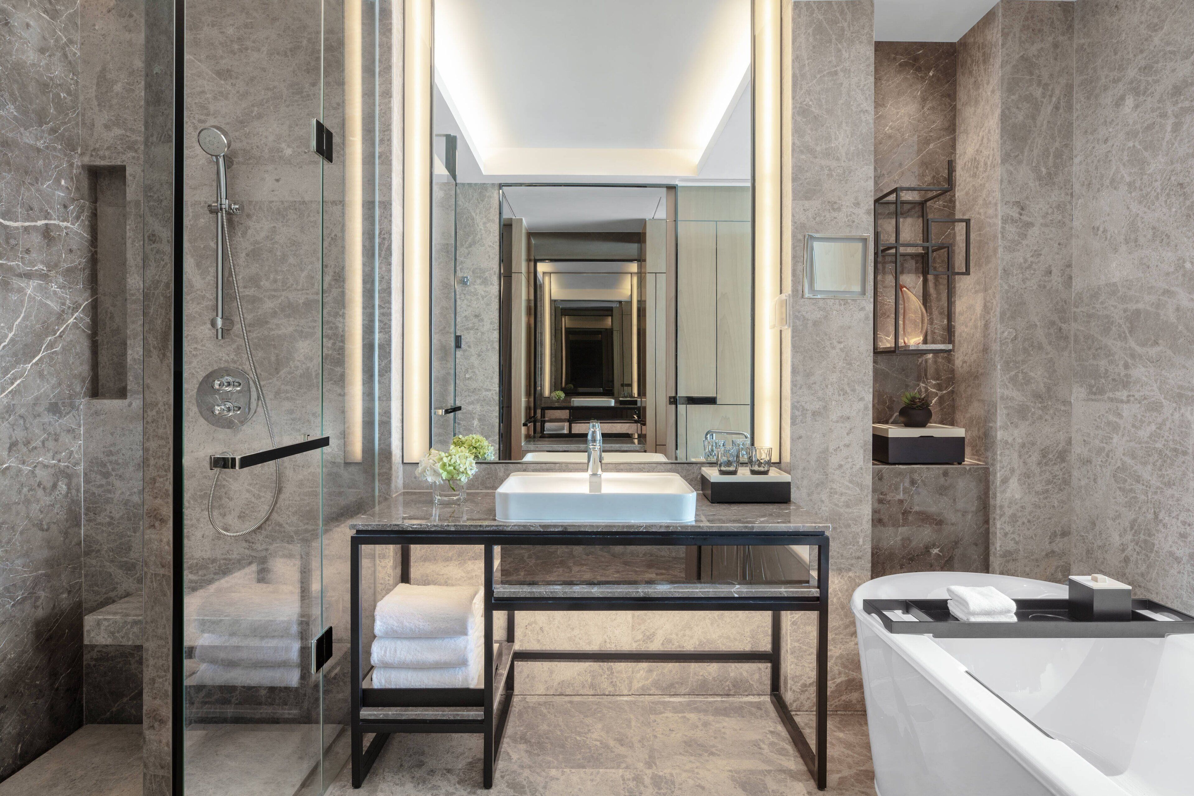 A modern bathroom with a glass-enclosed shower, a large mirror, a white sink, and a bathtub.