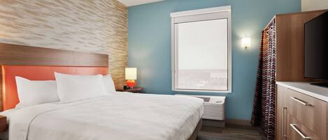 A hotel room with a bed, a nightstand, a TV, a window, and a wardrobe.