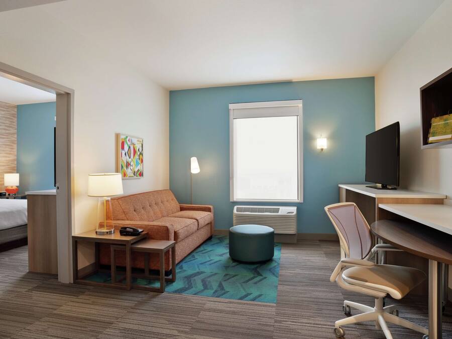Ein Hotelzimmer mit Bett, Sofa, Schreibtisch, Stuhl, Lampe, Fernseher und Fenster.