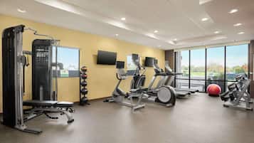 Un gimnasio con diversos equipos de ejercicio, una banca y un amplio ventanal con vistas al exterior.