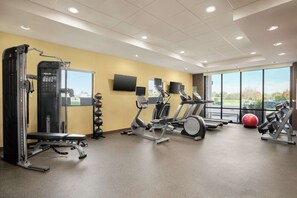 A gym with various exercise equipment, a bench, and a large window offering a view of the outdoors. - Home2 Suites by Hilton Warminster Horsham (Warminster)