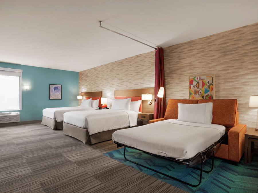 Une chambre d’hôtel avec deux lits, une fenêtre, une œuvre d’art accrochée au mur et une table de chevet avec une lampe.