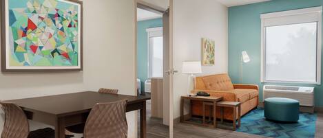 A hotel room with a dining area, a sofa, a lamp, and a large window.