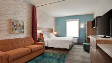 Una habitación de hotel con cama, sofá, televisor, escritorio y un cuadro en la pared.