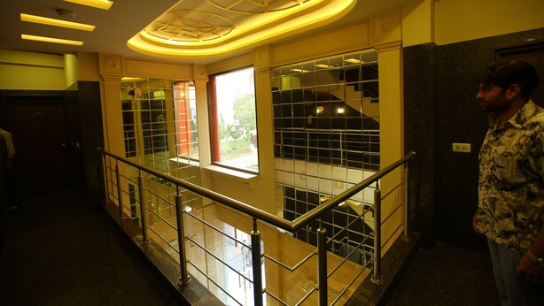 A hotel corridor with a glass railing, a decorative ceiling, and a window providing natural light. - Hotel Anandam (Gurugram)