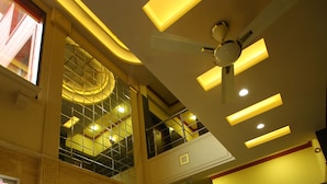A hotel lobby with a reception desk, a ceiling fan, and a decorative glass sculpture. - Hotel Anandam (Gurugram)